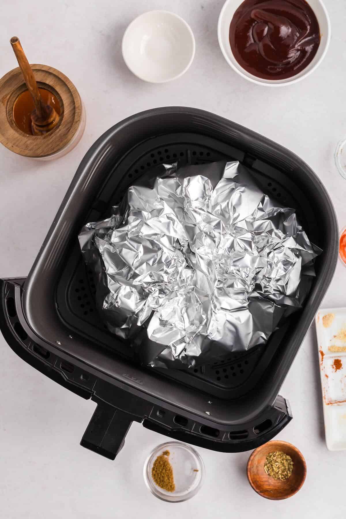 Air Fryer pulled pork with the roast wrapped tightly in foil in an air fryer basket.