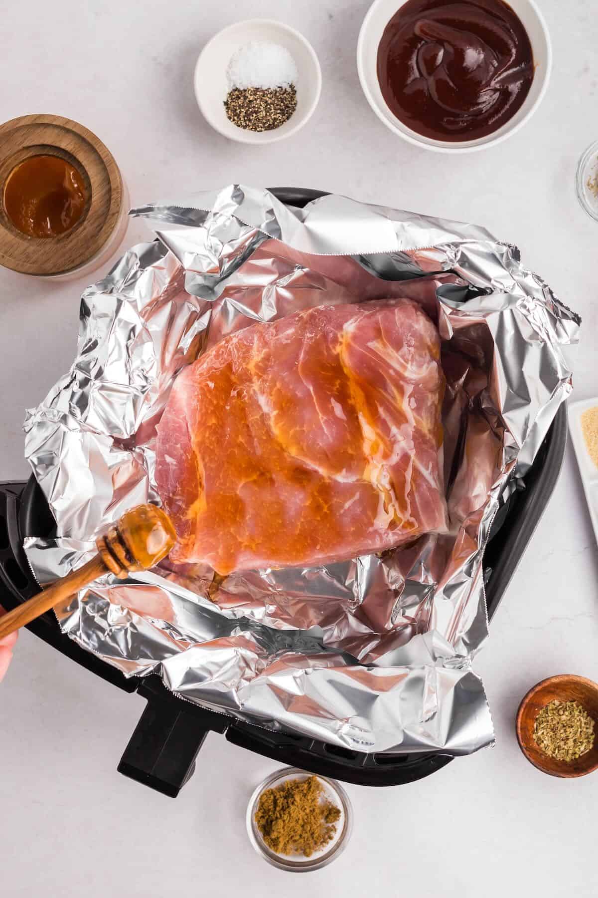 Pulled pork in foil in an air fryer basket topped with honey and other seasonings.