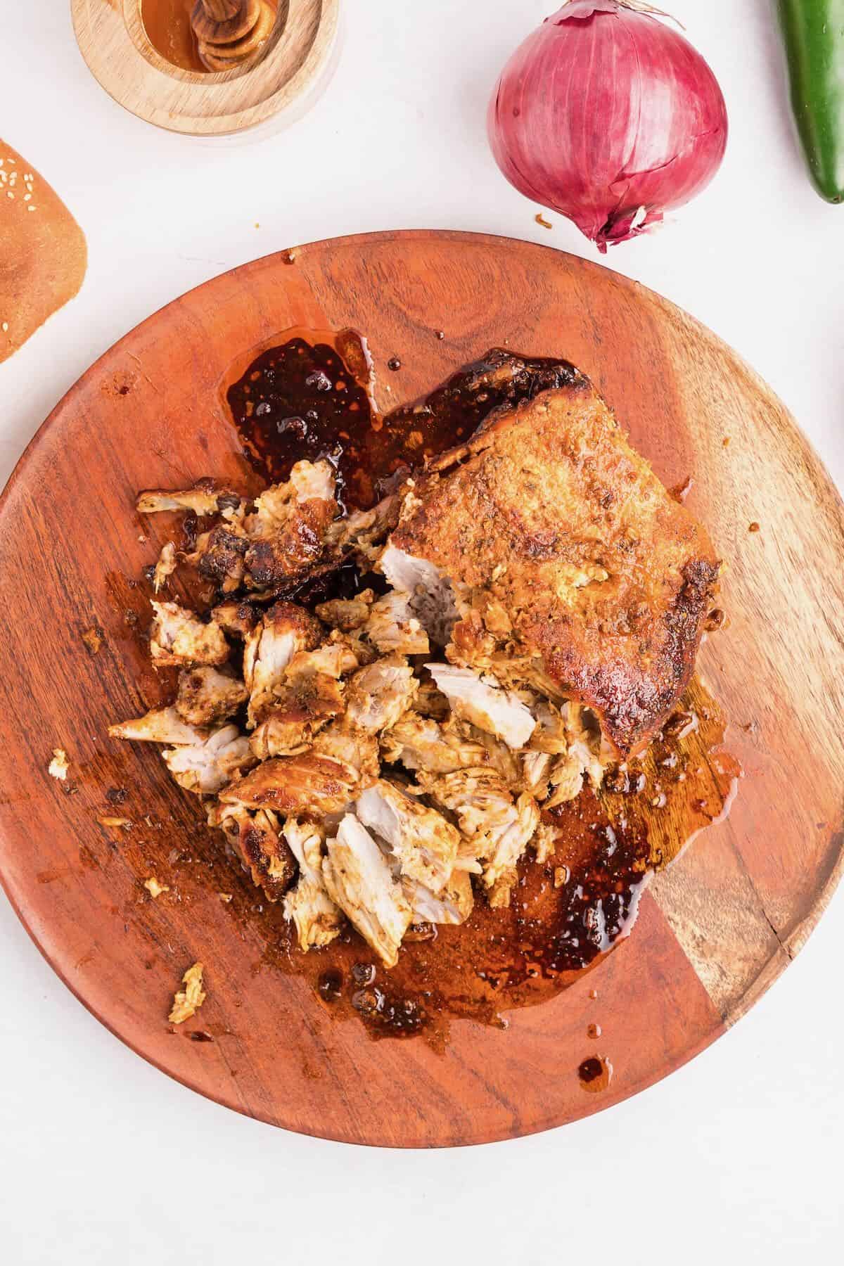 A pork butt cooked in an air fryer on a cutting board with the meat being shredded.