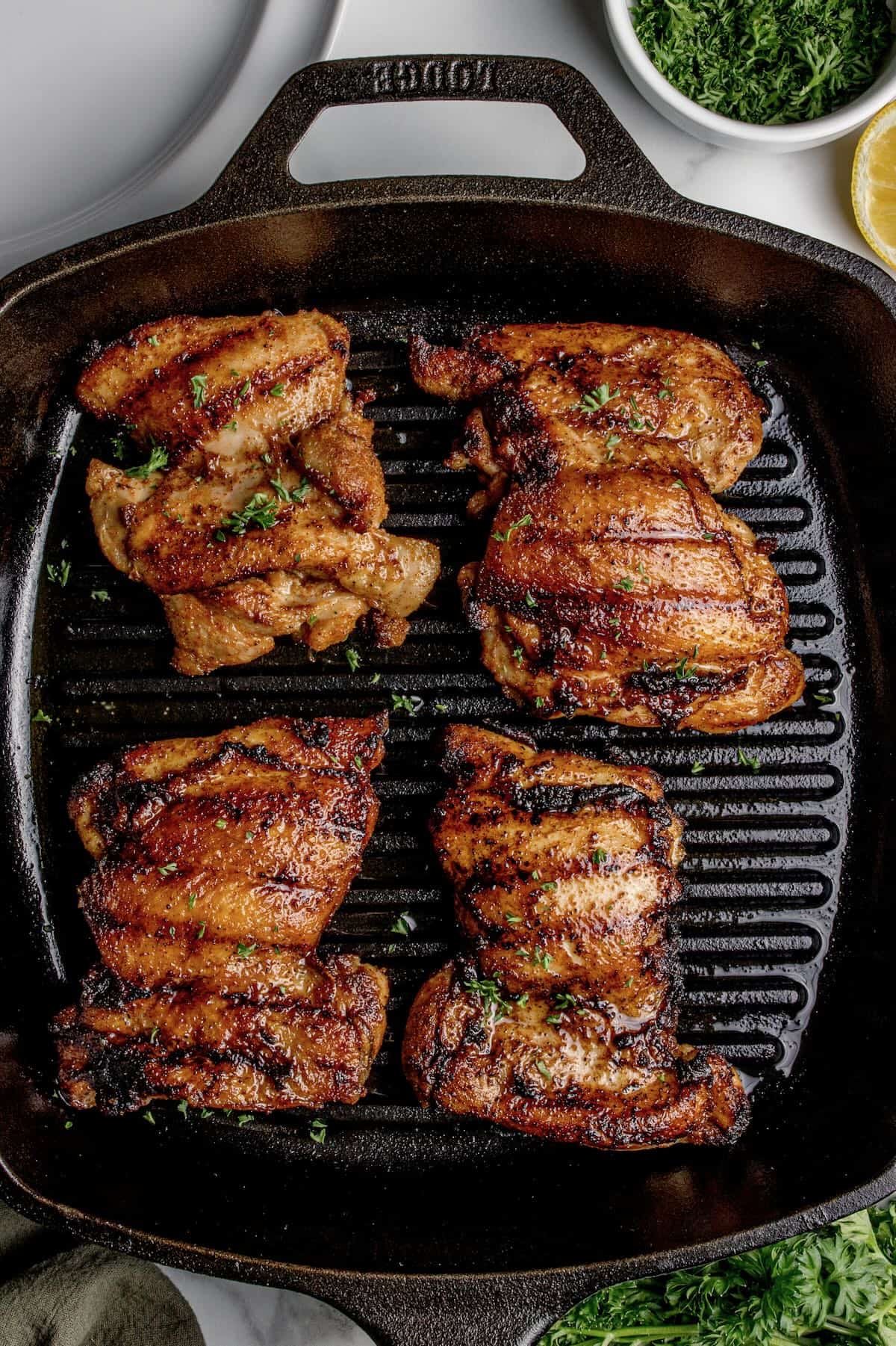 Four chicken thighs are cooking on the stove in a grill pan.