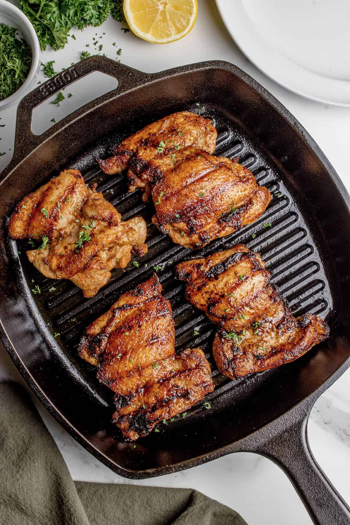 Four chicken thighs grilled in a square cast-iron grill pan.