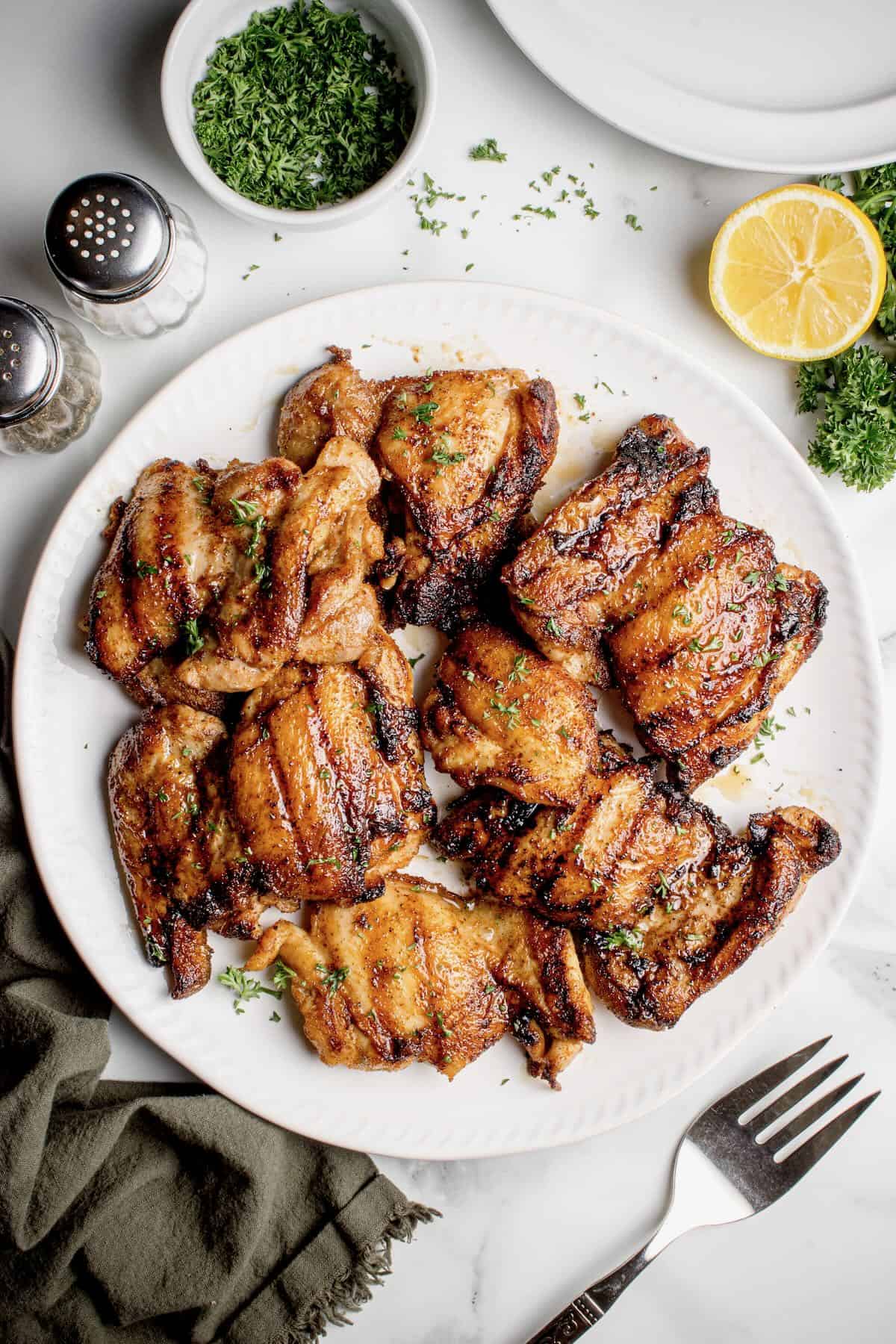 A white plate full of grill pan chicken thighs with grill marks.