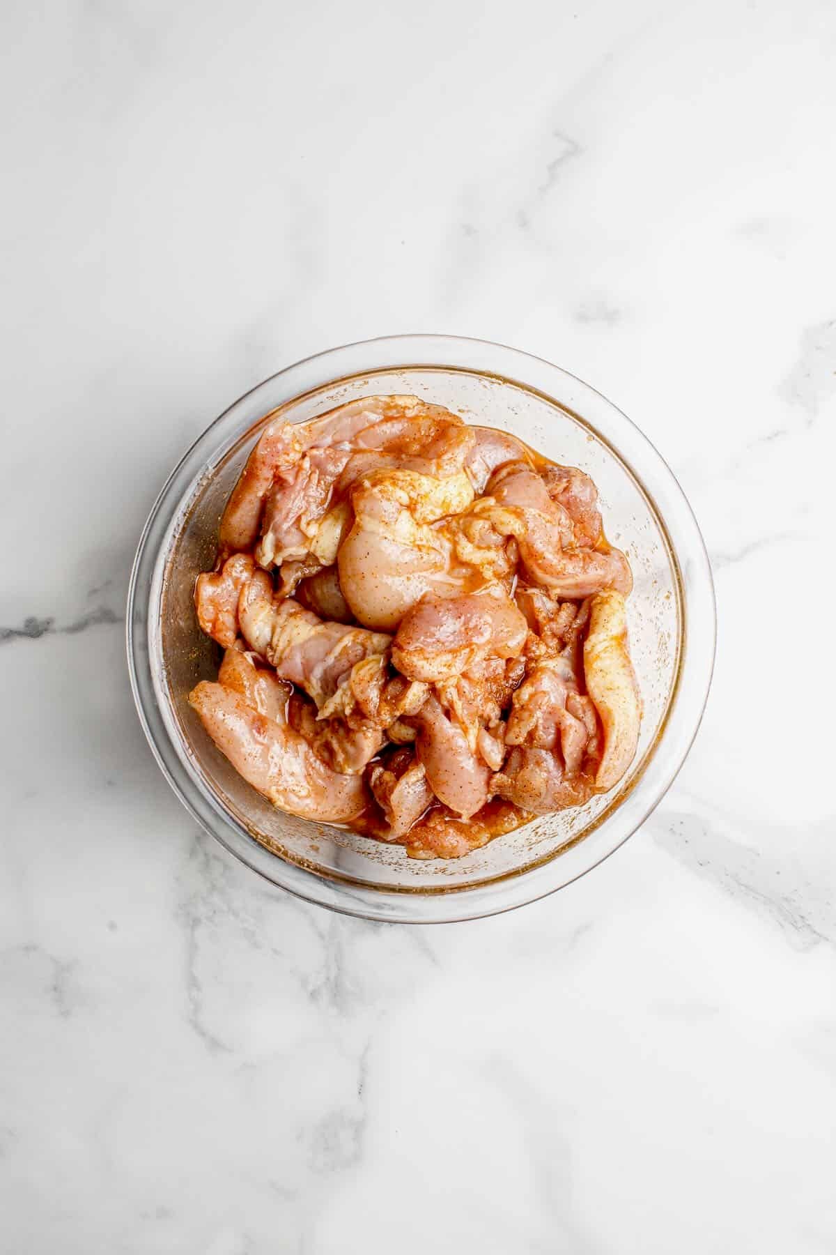 Chicken thighs marinating in a bowl with a marinade consisting of oil, paprika, onion, and garlic powder.