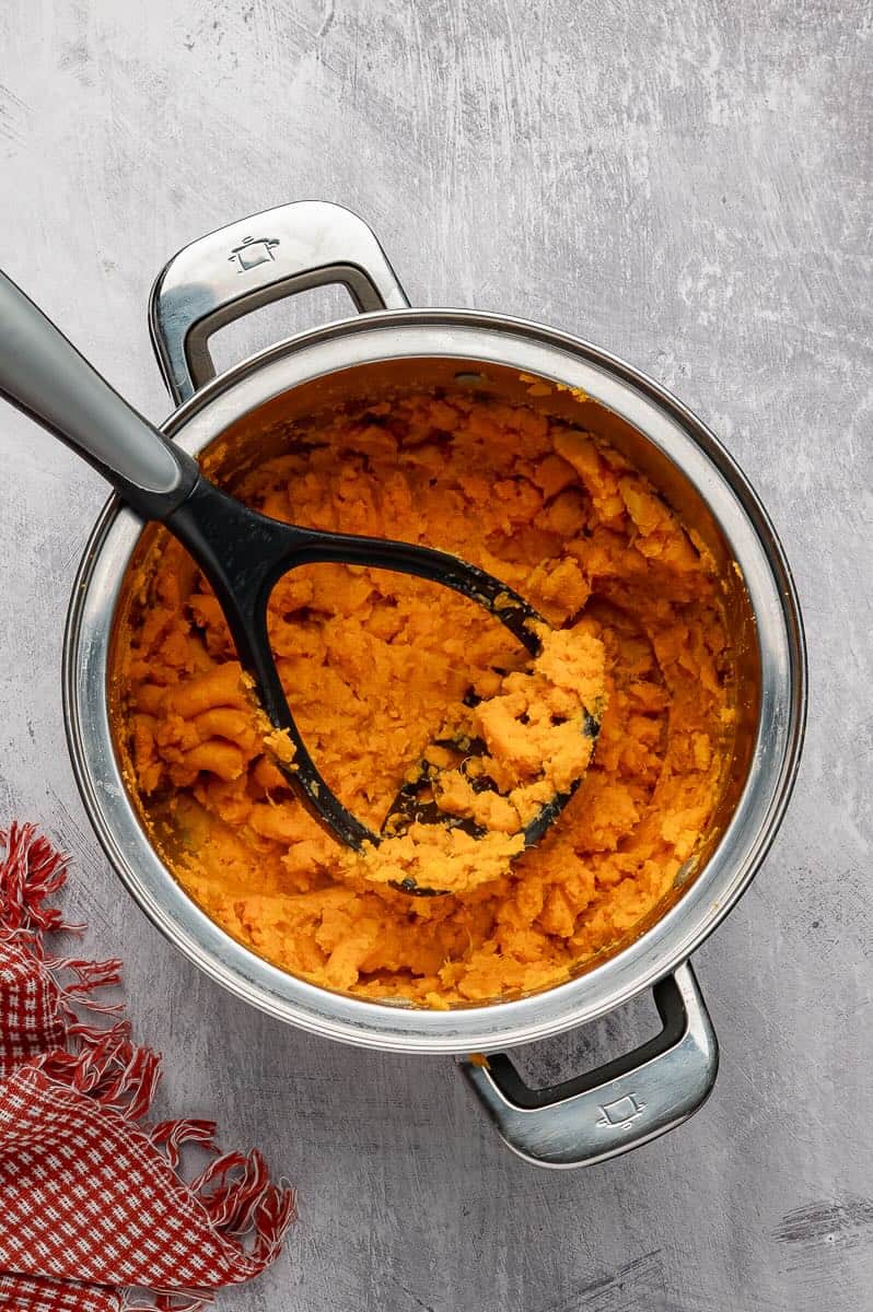 Using a potato masher to mash sweet potatoes.