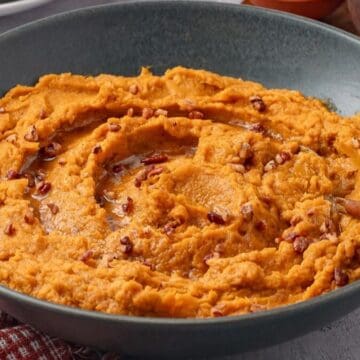 Savory mashed sweet potatoes in a bowl topped with brown butter and roasted pecans.