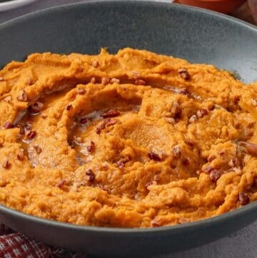 Savory mashed sweet potatoes in a bowl topped with brown butter and roasted pecans.