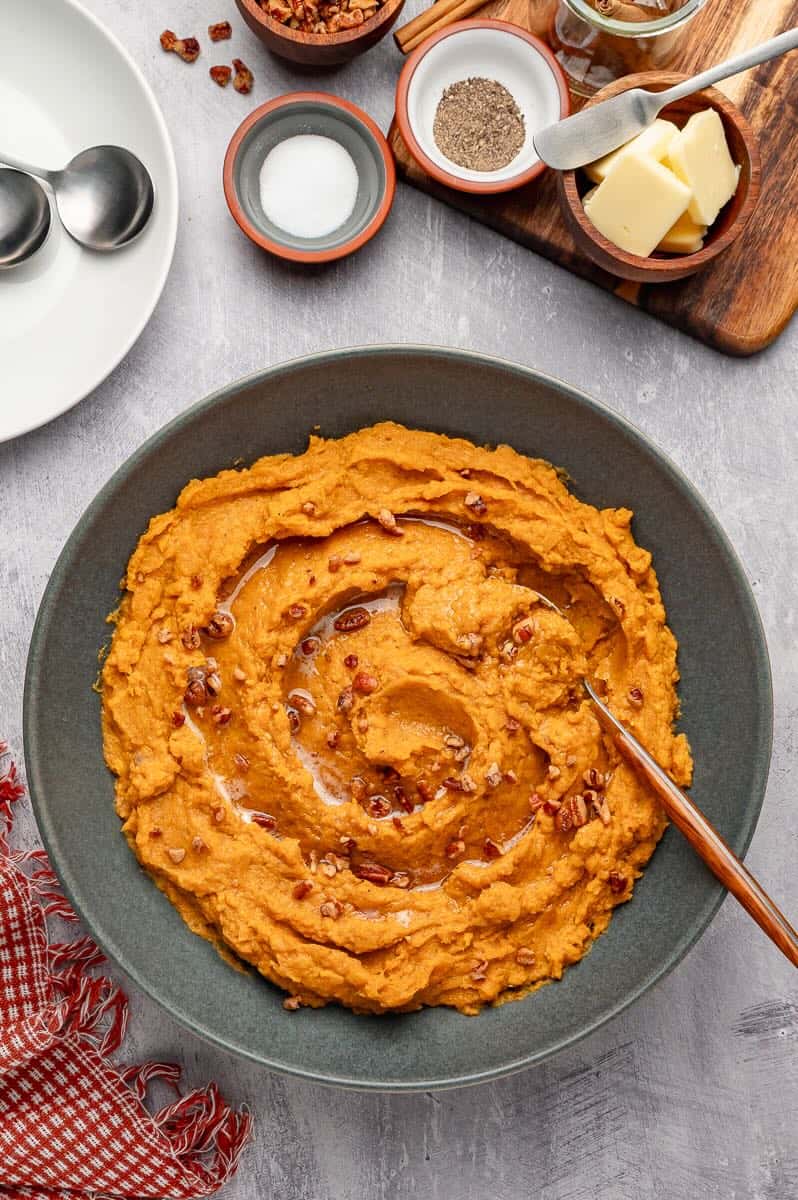 Savory mashed sweet potatoes with brown butter topped with roasted pecans in a serving bowl
