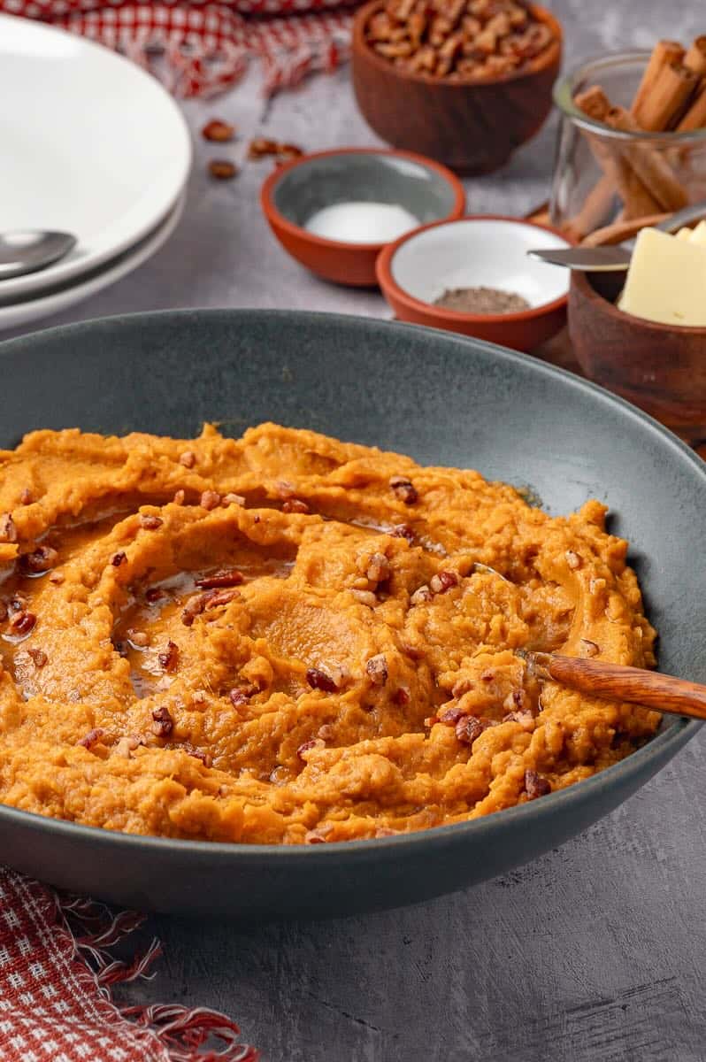 Savory mashed sweet potatoes in a grey bowl with a spoon in it.