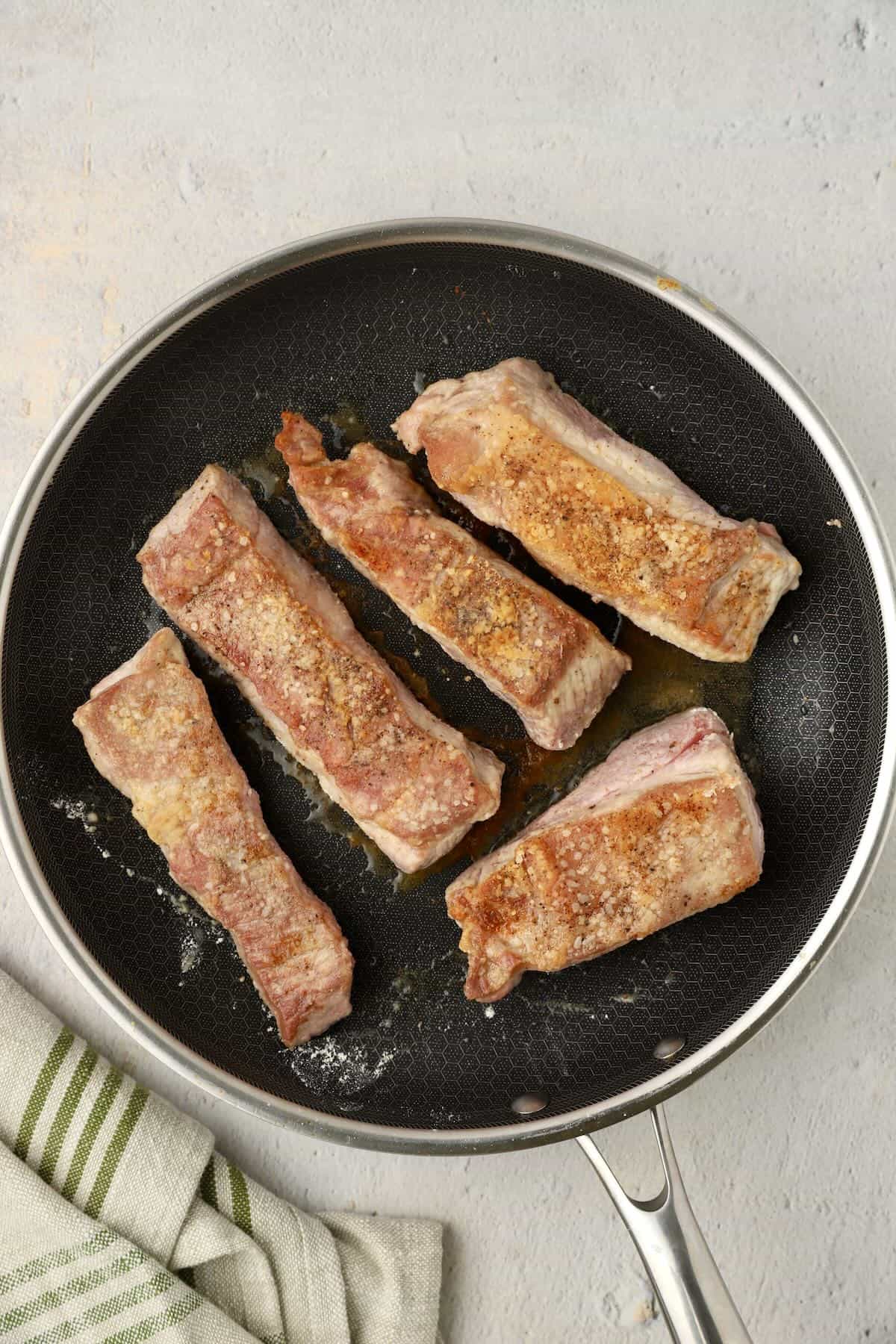 Floured boneless country style pork ribs in a skillet browning.