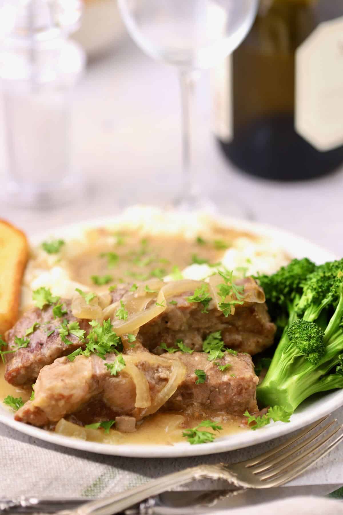 Slow Cooker Country Style Ribs topped with Vidalia Onion Gravy on a plate with mashed potatoes and broccoli.