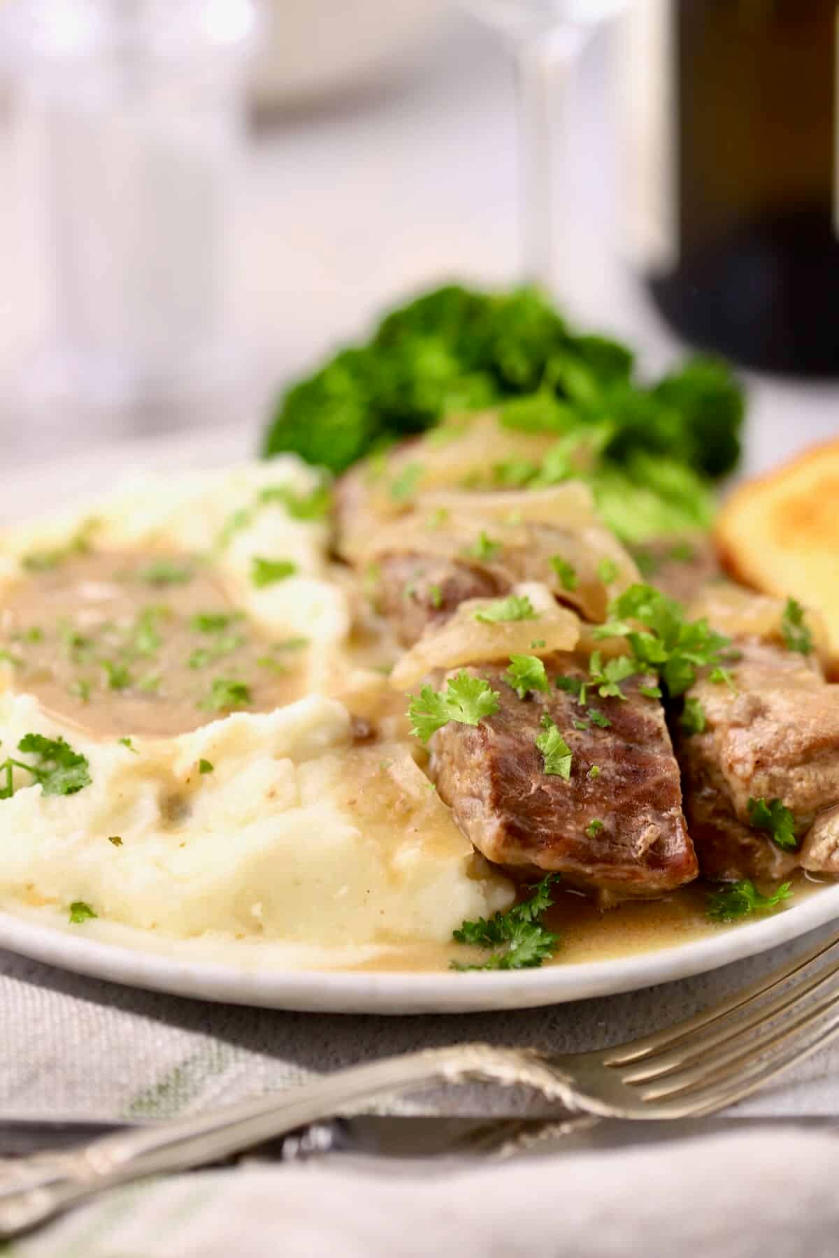 Slow cooker country style ribs on a plate topped with Vidalia onion gravy served with mashed potatoes and broccoli.