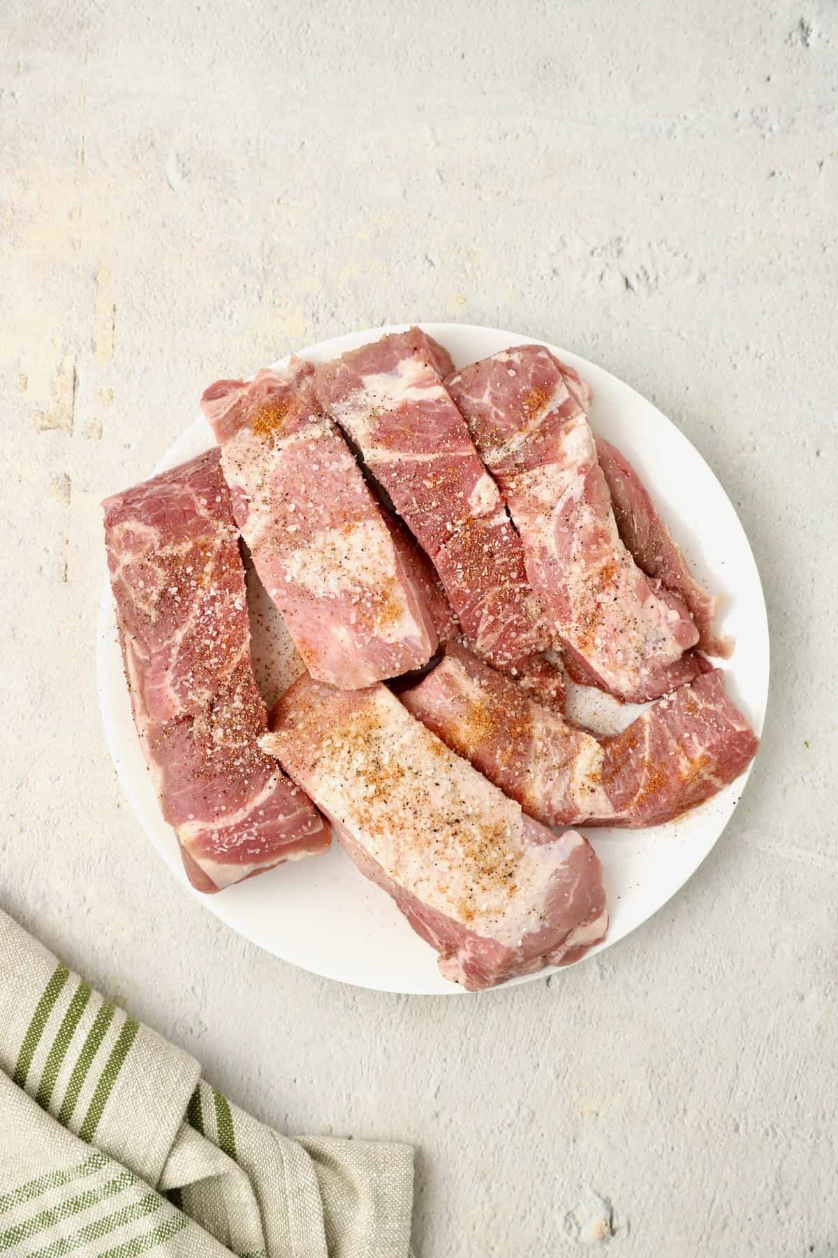 Country style pork ribs on a plate seasoned with Cajun seasoning and pepper.