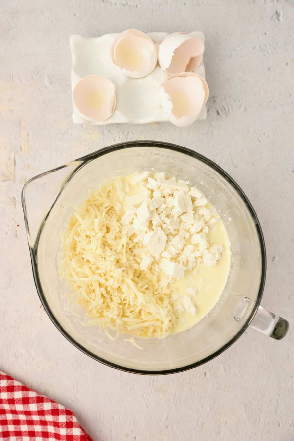 Eggs, cream and three types of cheeses in a mixing bowl.