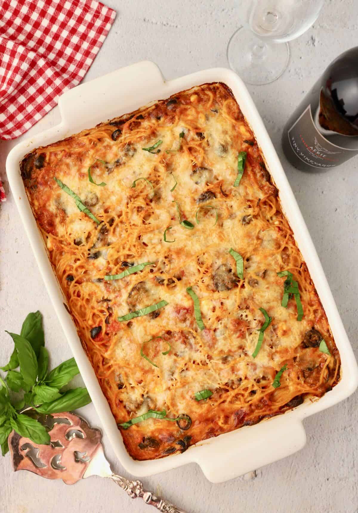 Baked spaghetti pie casserole in a white baking dish garnished with strips of basil.