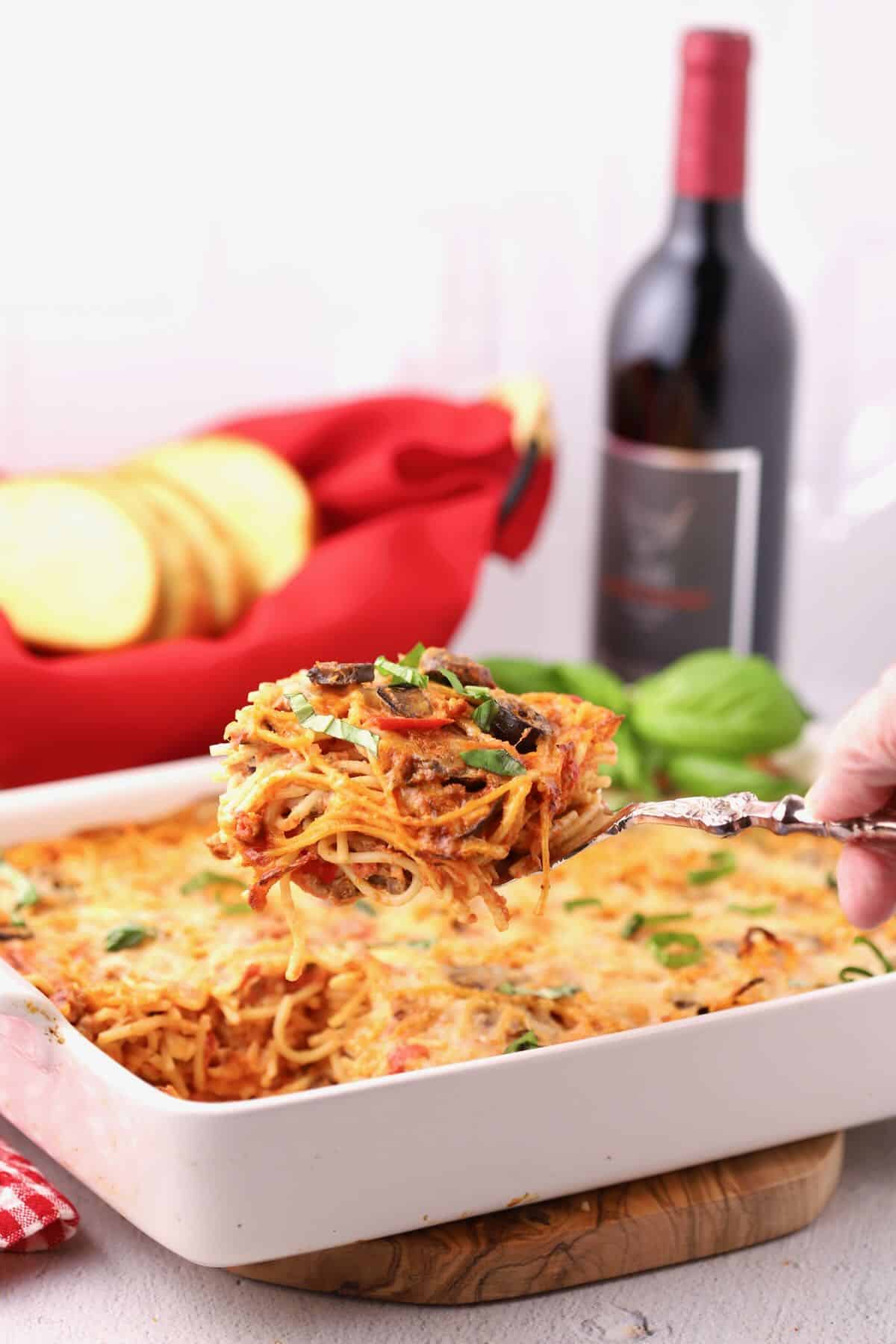 Baked spaghetti pie casserole in a white baking dish with a large serving being taken out.