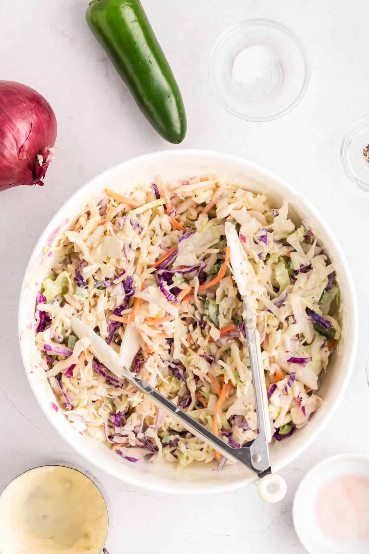 Spicy coleslaw being tossed with dressing in a white bowl.