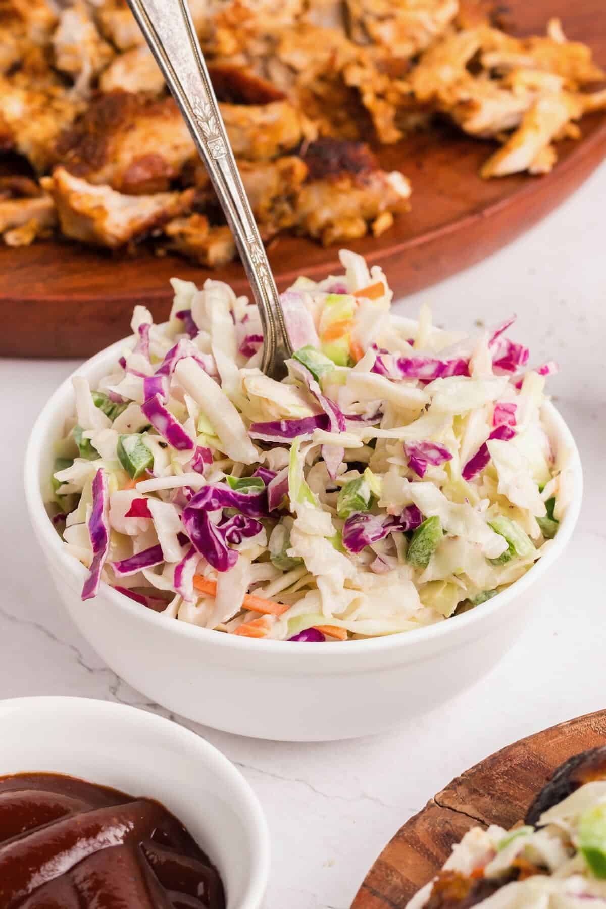 A white bowl full of spicy coleslaw with a fork.