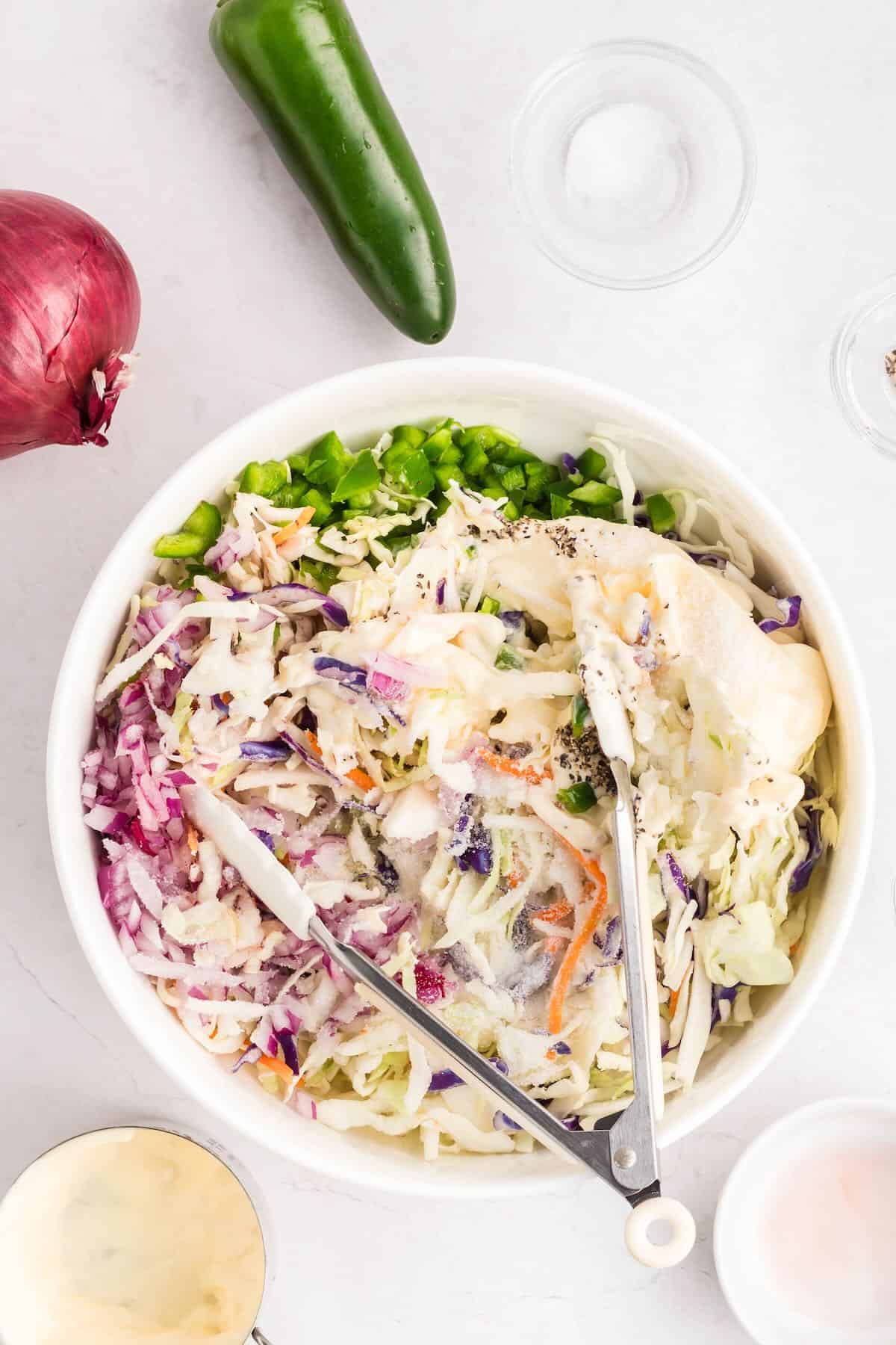 A large bowl with coleslaw and dressing, and a pair of tongs.