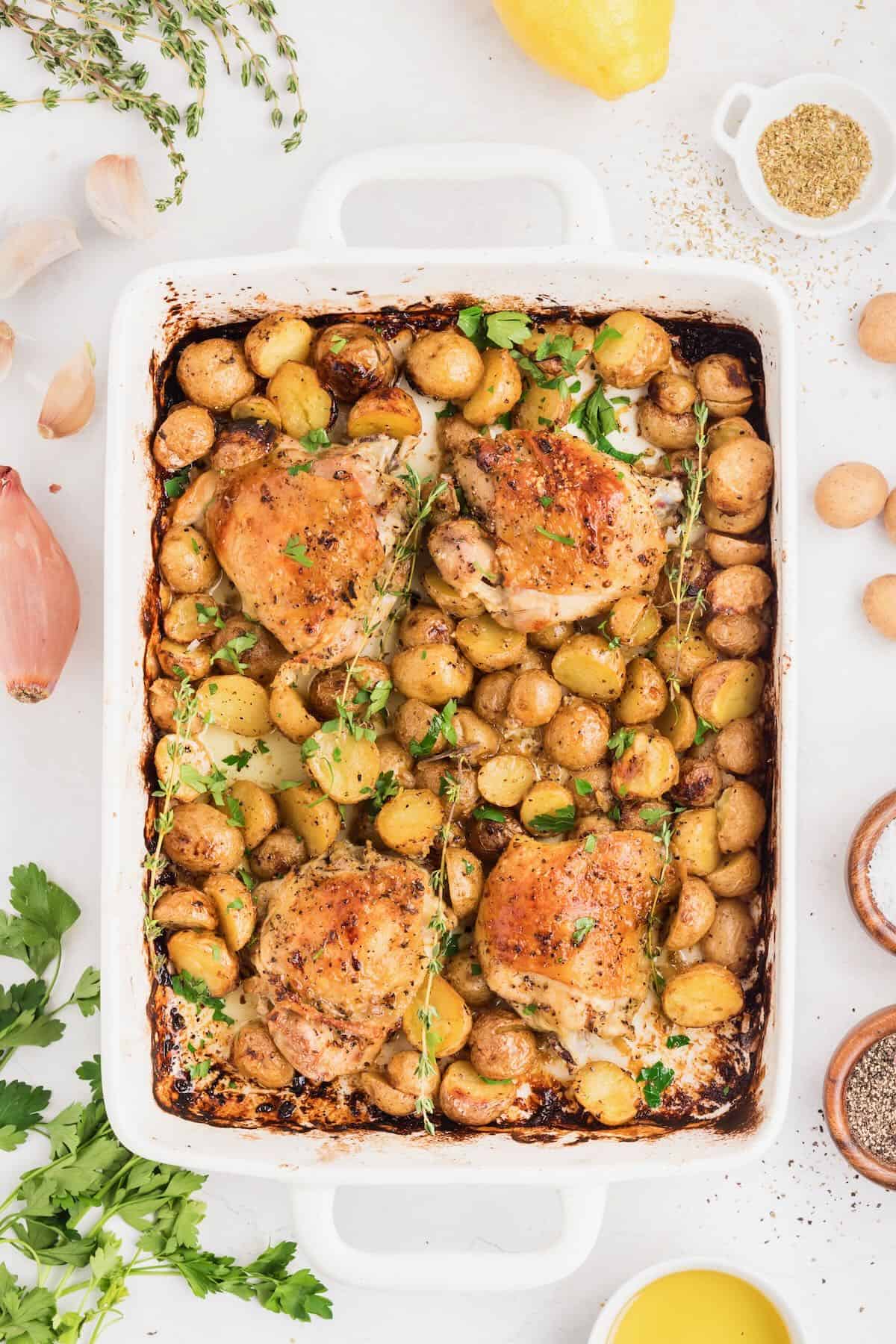 A white baking dish with baked crispy chicken thighs and baby potatoes.