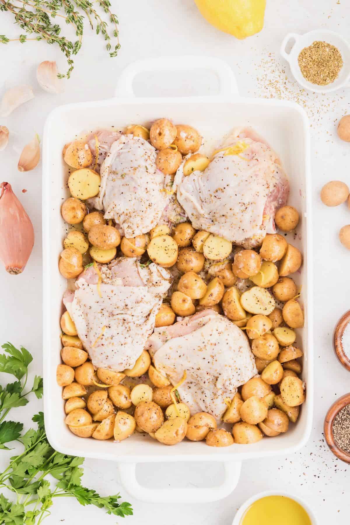 A baking dish with raw chicken thighs and baby potatoes.