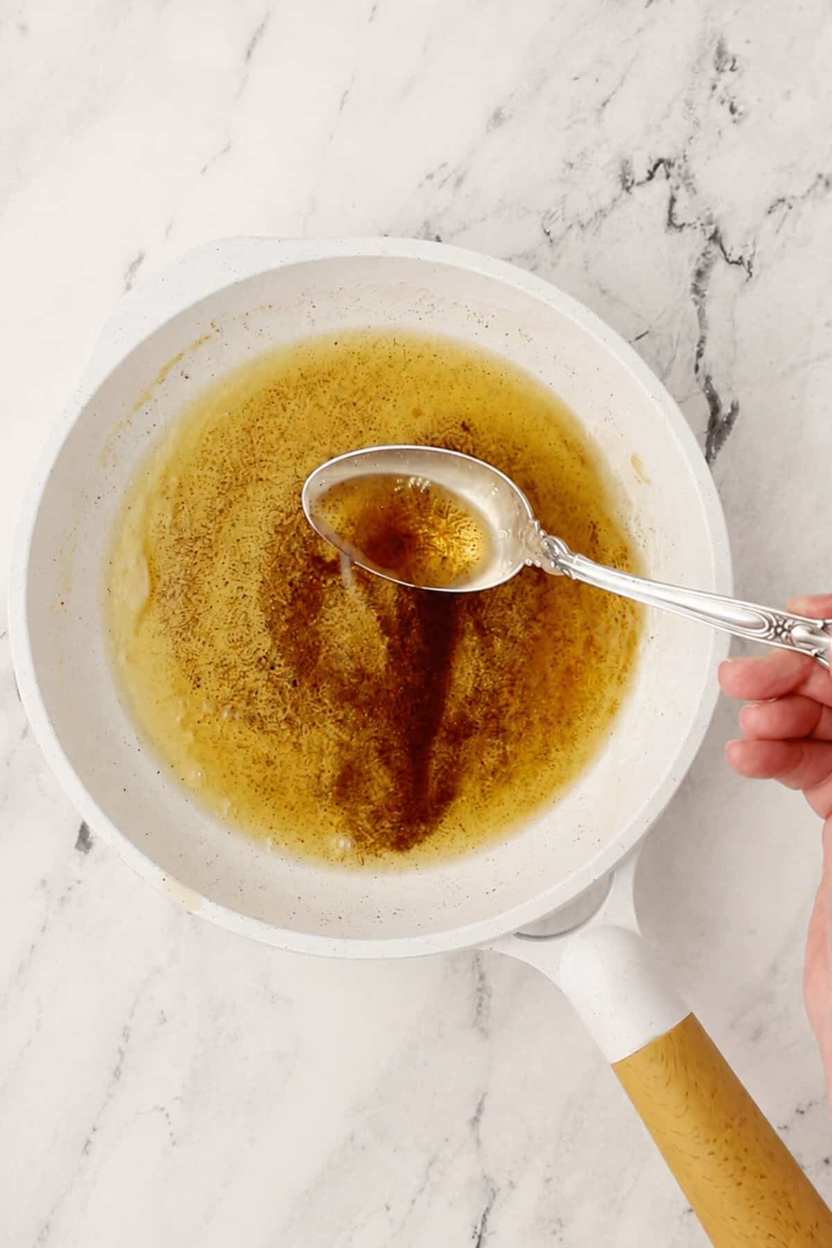 A light colored skillet with brown butter and a spoon.