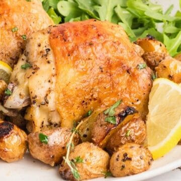 Crispy baked chicken thigh and baby potatoes on a plate, garnished with lemon slices.