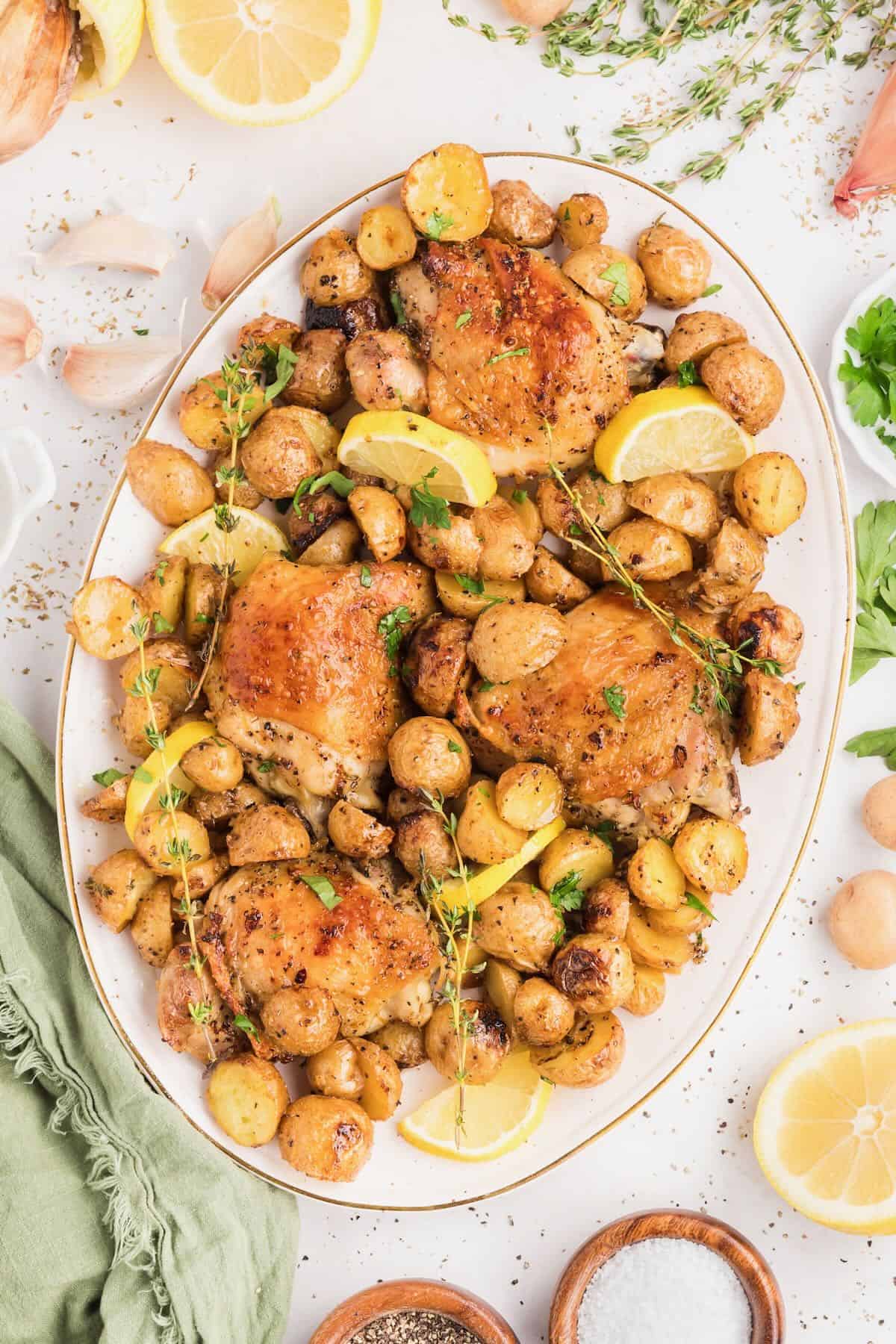 Baked chicken thighs and potatoes piled high on a white serving platter.