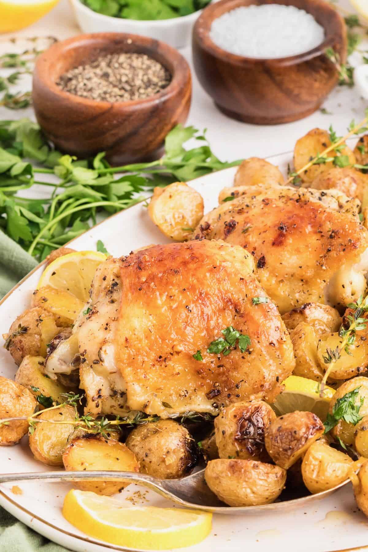 A plate with crispy baked chicken thighs and baby potatoes, garnished with lemon slices and thyme.