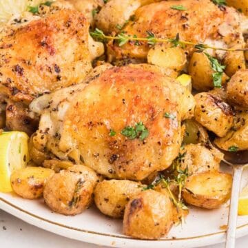 A crispy baked chicken thighs on a plate surrounded by baby potatoes.