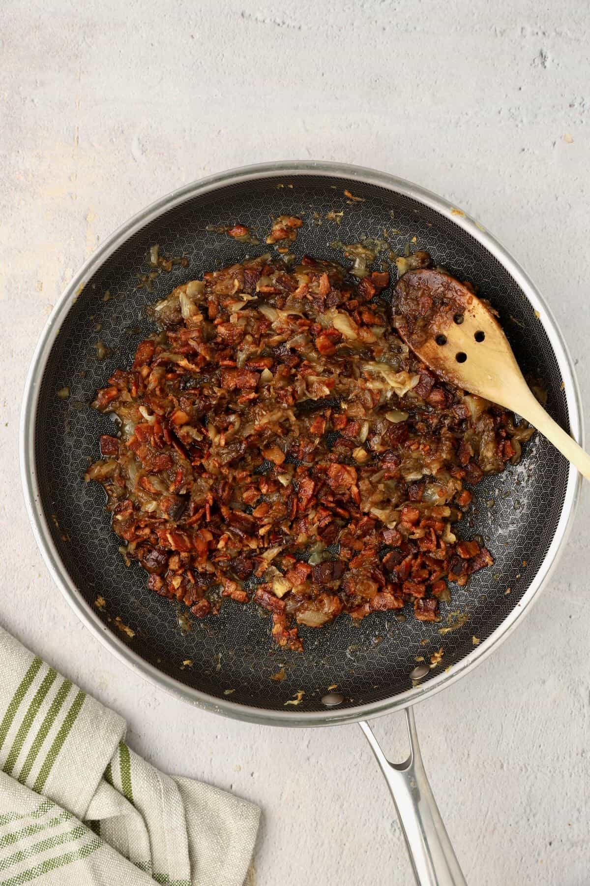A skillet with caramelized onions, with cooked bacon added.