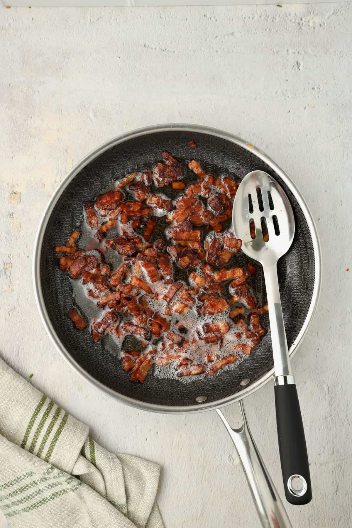 Golden brown small pieces of thick bacon cooking in a skillet.