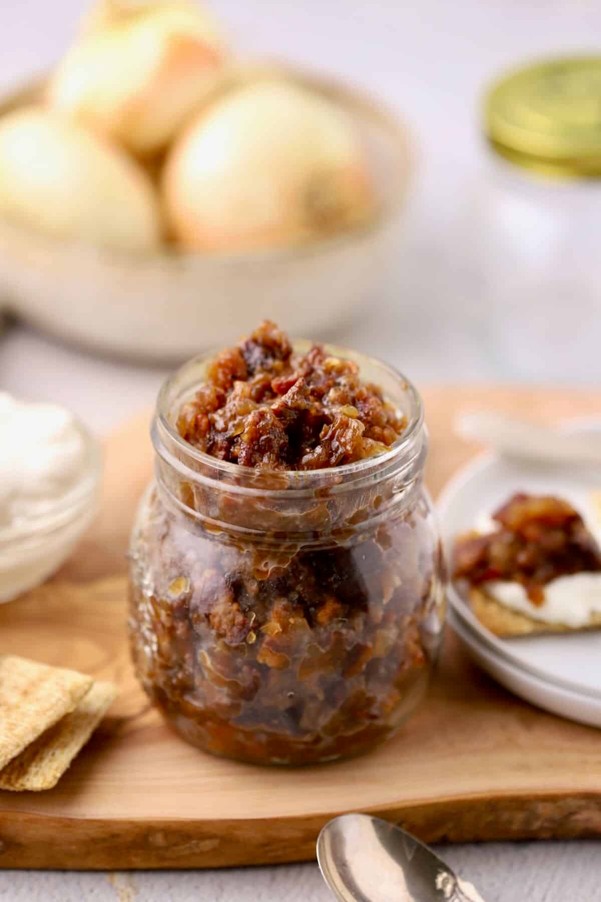 A jar full of bourbon bacon onion jam on a cutting board.