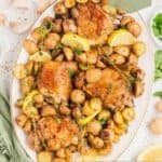 An oval serving platter pilled high with baked chicken thighs and baby potatoes.