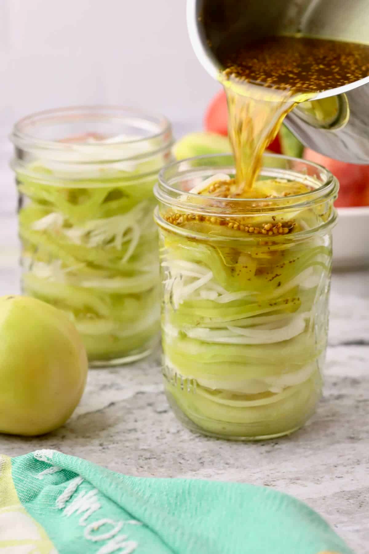 Pint size jars full of sliced green tomatoes and onions with brine poured over the contents.