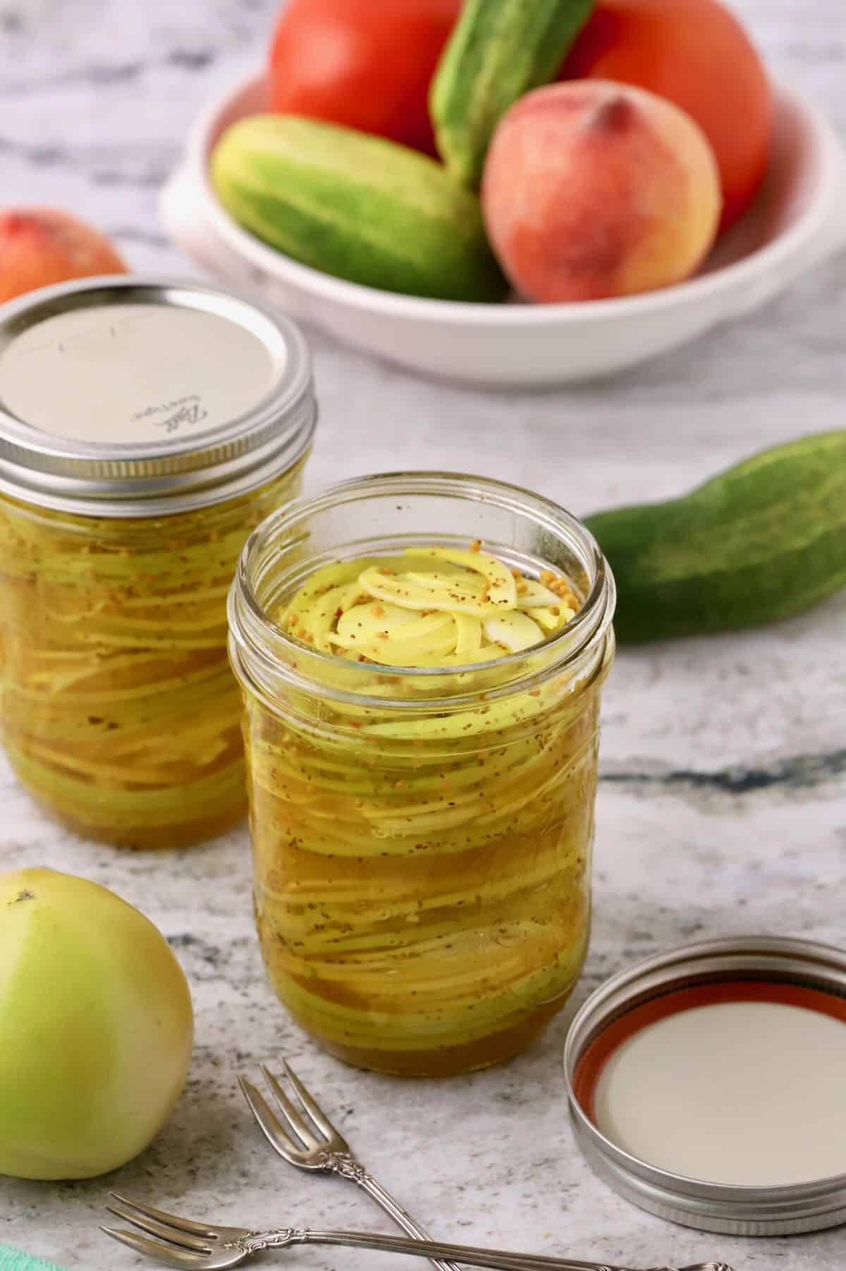 Two pint size jars full of pickled green tomatoes and onions with brine.