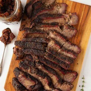 Slices of smoked chuck roast on a cutting board with bourbon bacon onion jam.
