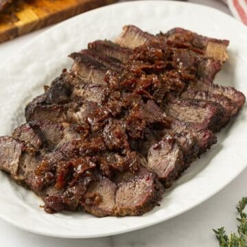 Slices of smoked chuck roast topped with bourbon bacon onion jam on a platter.