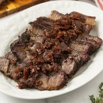 Slices of smoked chuck roast topped with bourbon bacon onion jam on a platter.