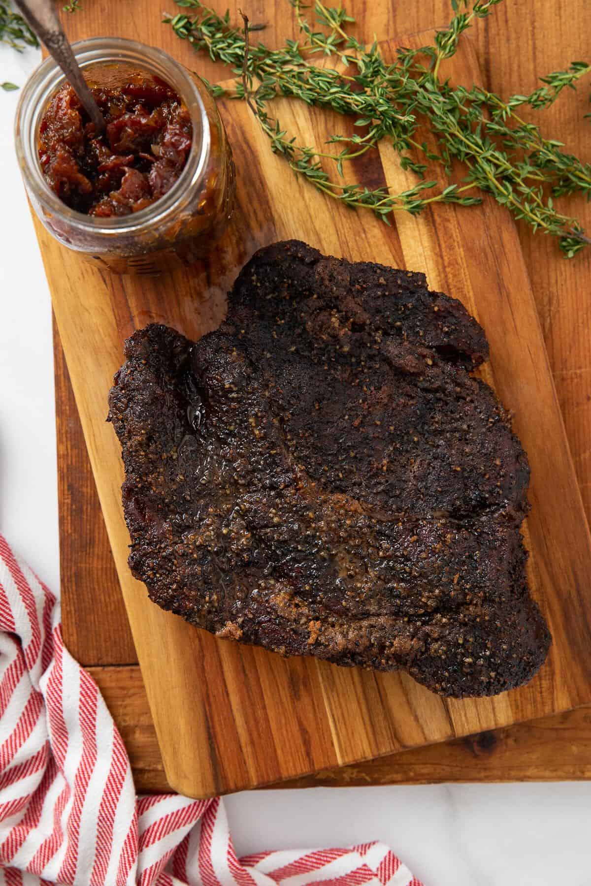 A whole smoked chuck roast on a cutting board after smoking with a jar of bacon jam.