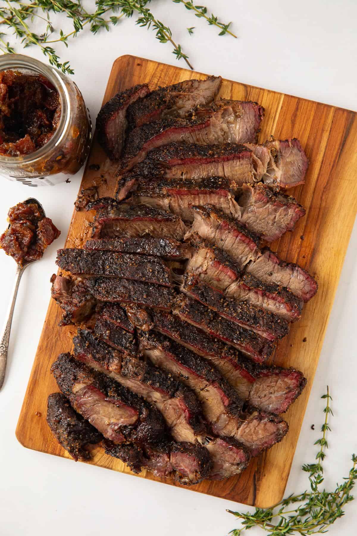 Sliced juicy smoked chuck roast on a cutting board with bourbon bacon onion jam.