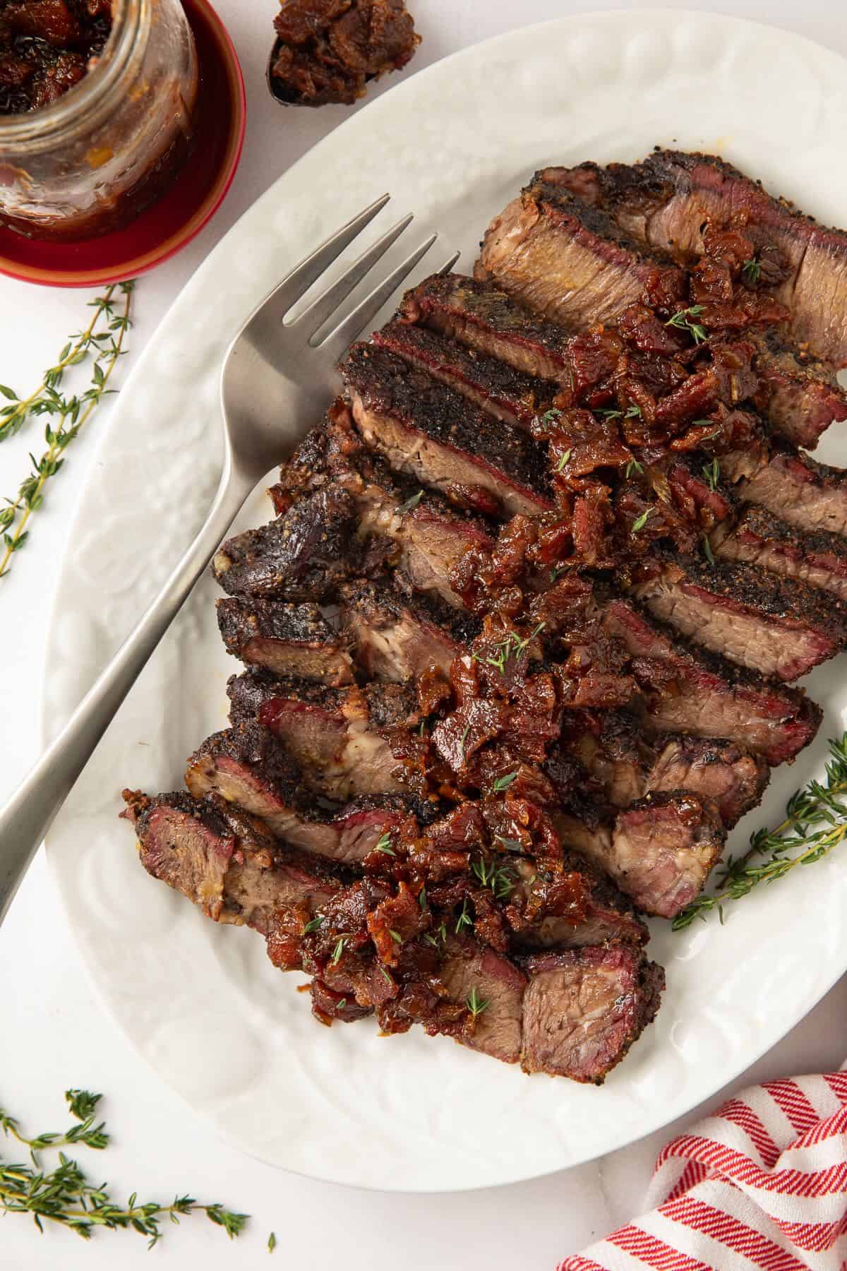 Sliced smoked chuck roast topped with bourbon bacon onion jam on a white serving platter.