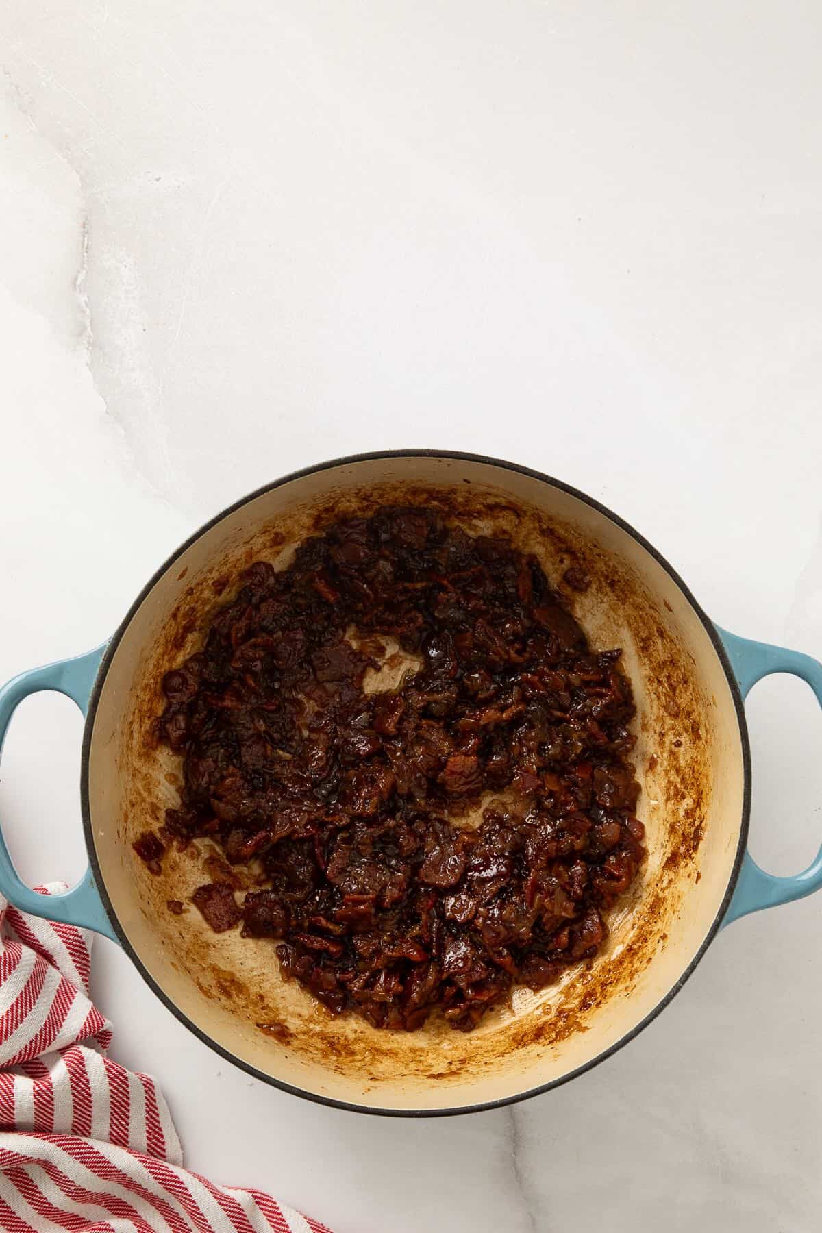Dutch oven with caramelized onions, cooked bacon, and other ingredients to make bourbon bacon onion jam.