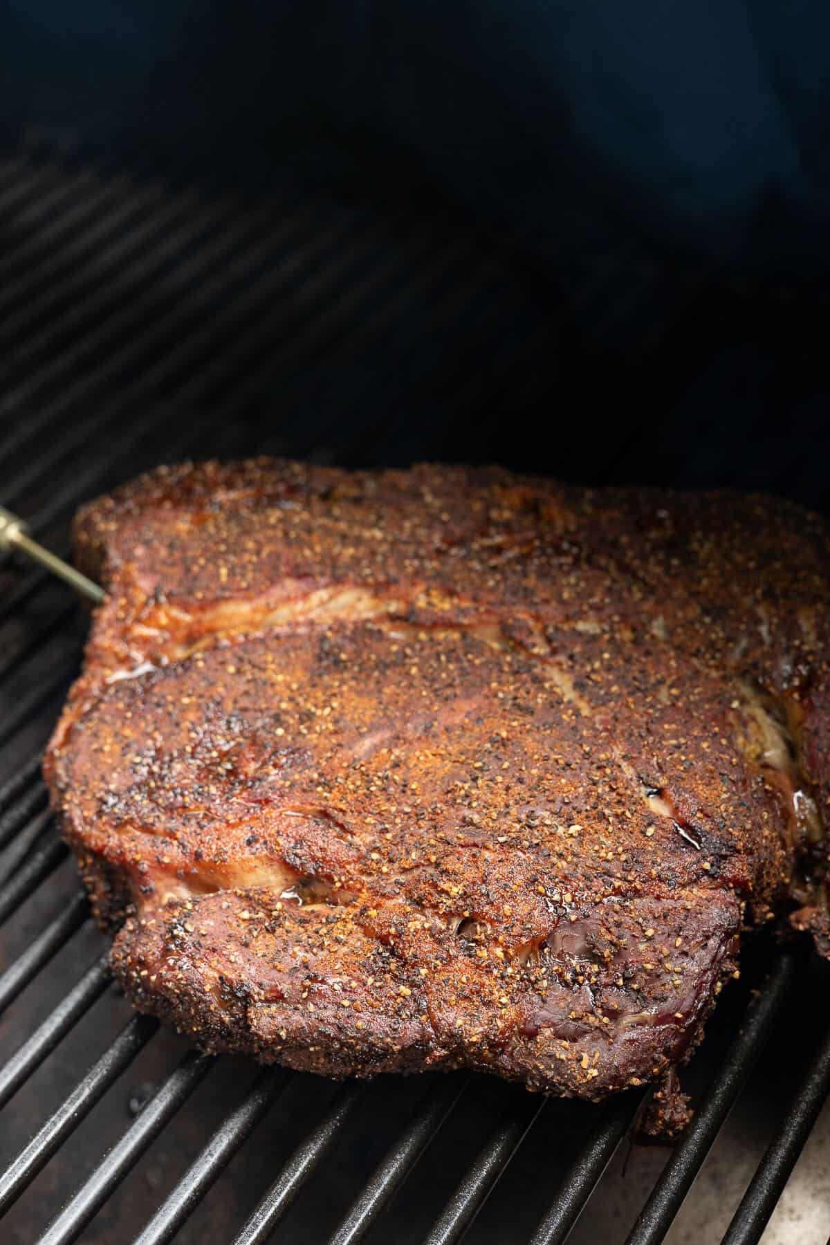A chuck roast coated with a dry brine is smoking in a smoker.
