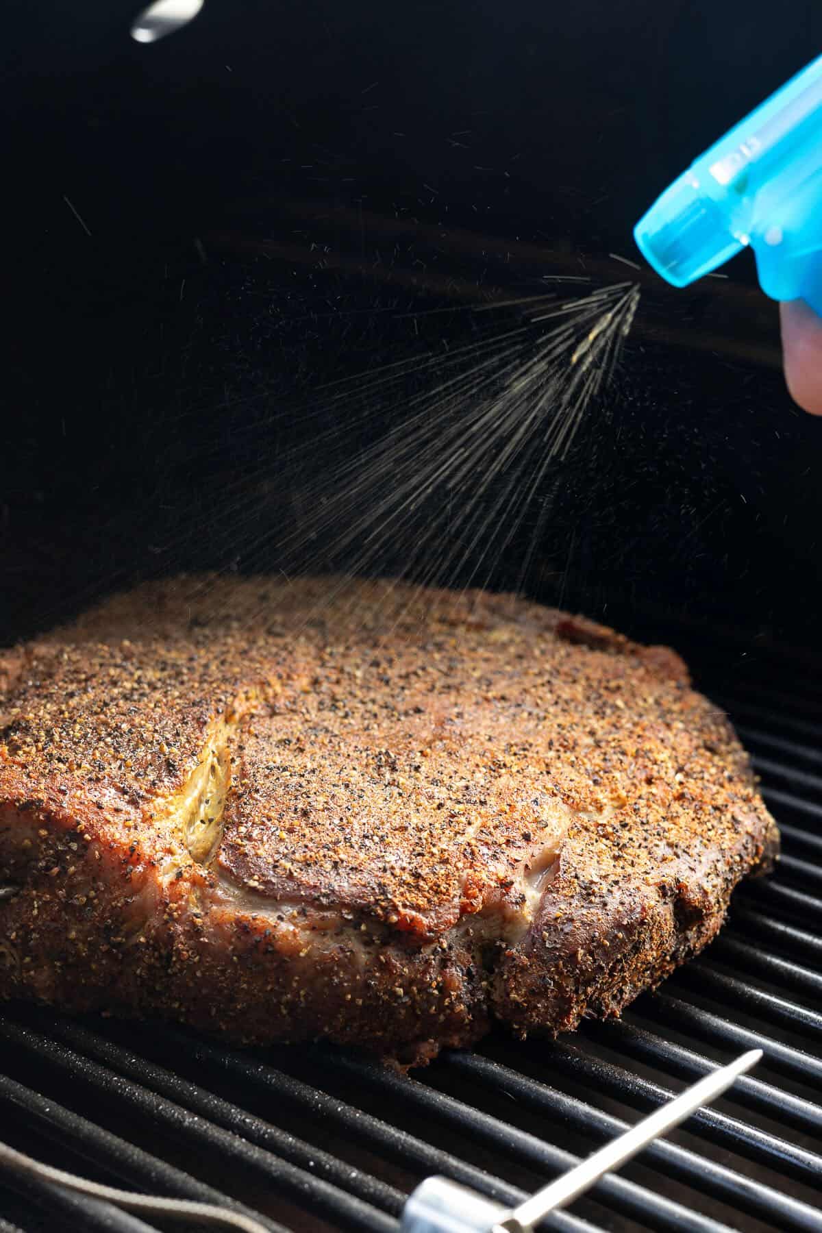 Spritzing a smoking chuck roast with a liquid while smoking.