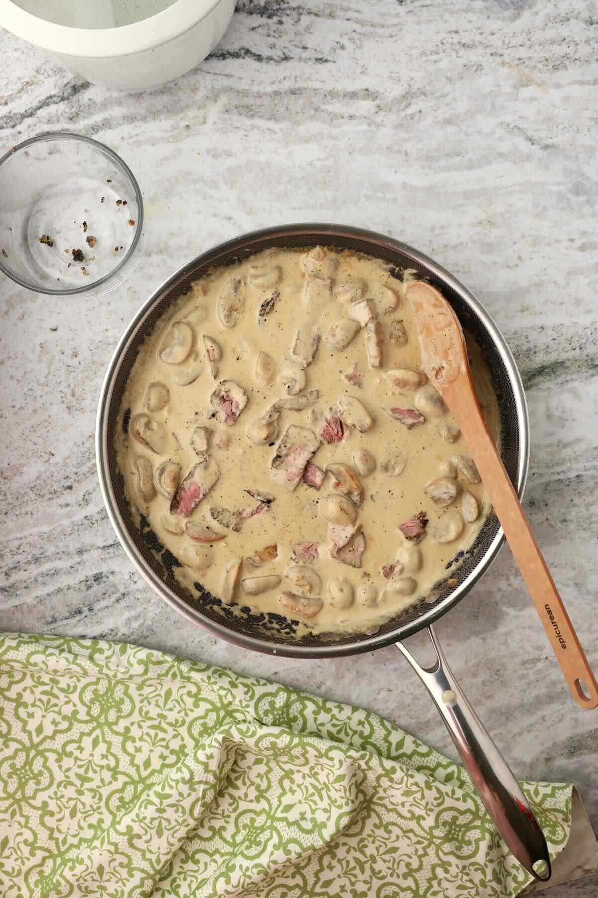 Beef stroganoff in a skillet with sour cream sauce, slices of beef, and mushrooms.