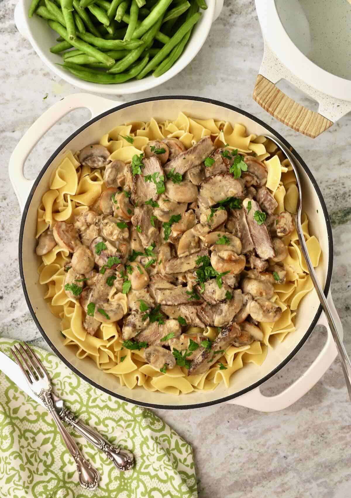 Beef Stroganoff served over egg noodles in a skillet, garnished with chopped parsley.