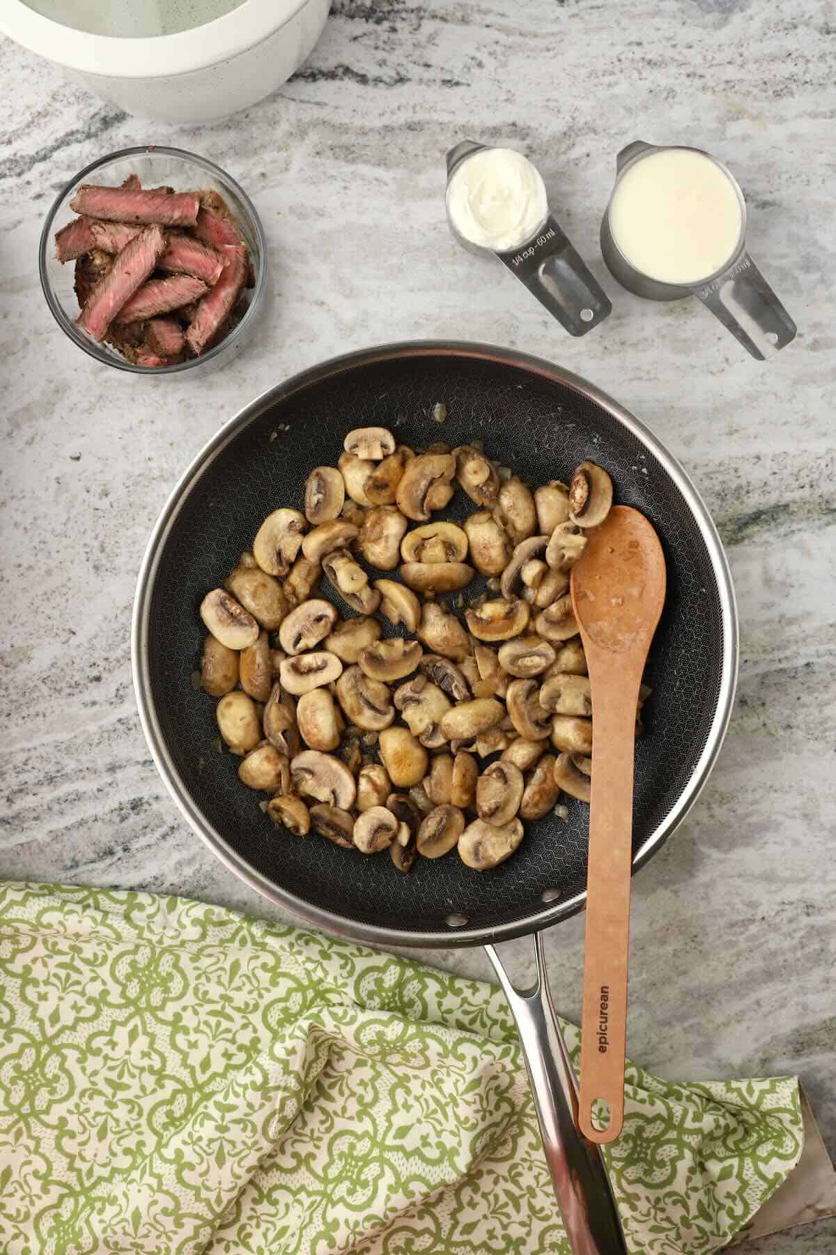 Sliced mushrooms are cooking in a skillet.