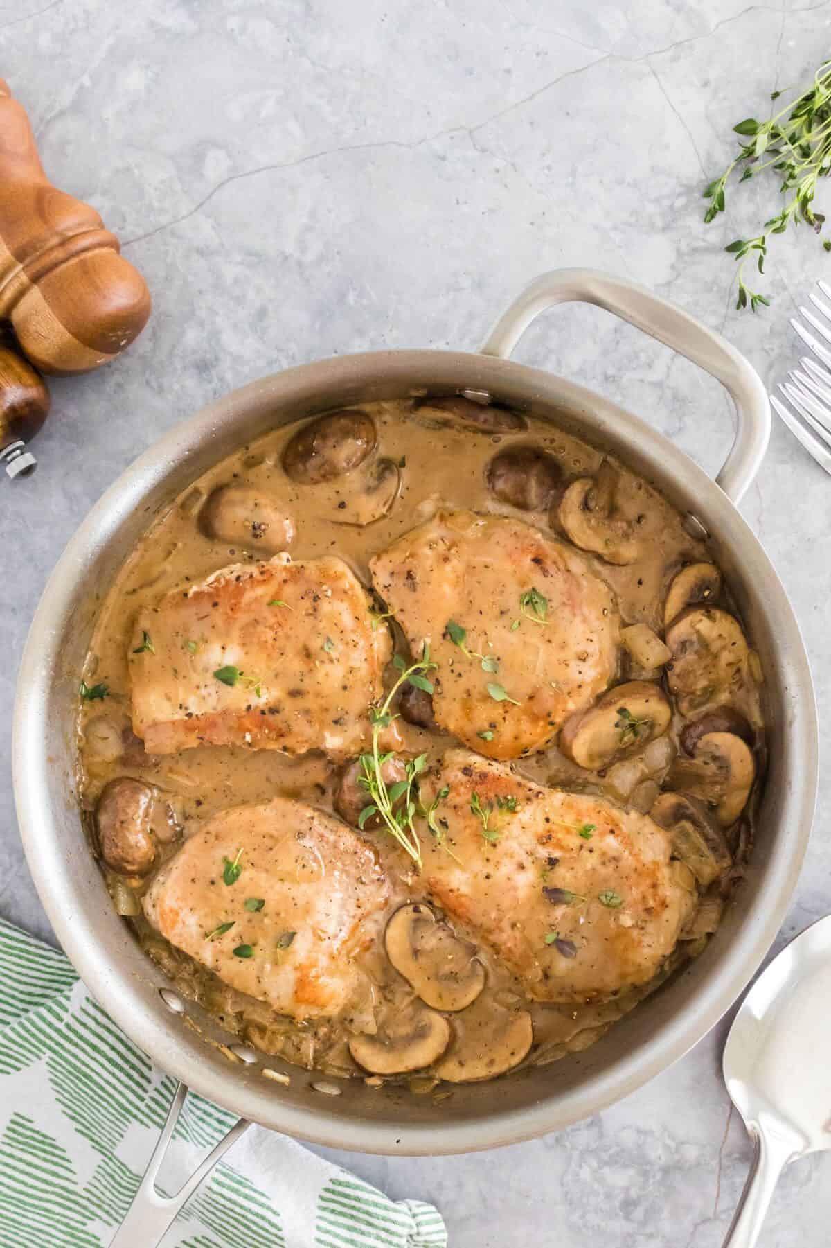 Creamy mushroom pork shops in a skillet with pan seared chops, mushrooms and a creamy pan sauce.