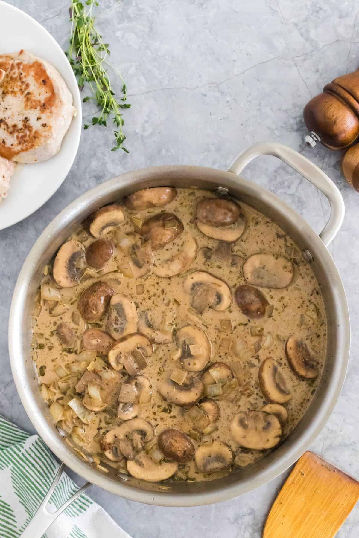 Making the pan sauce for the pork chops by adding chicken stock, balsamic vinegar, and heavy cream.