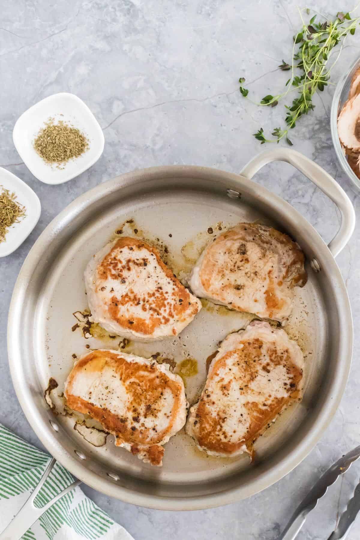 Four boneless pork chops being pan seared in a skillet.